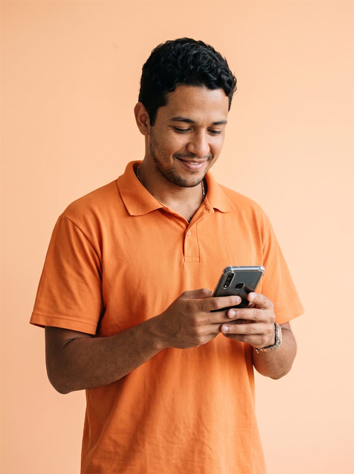 Imagem ilustrativa: homem jovem de camisa polo laranja, sorrindo enquanto olha o celular