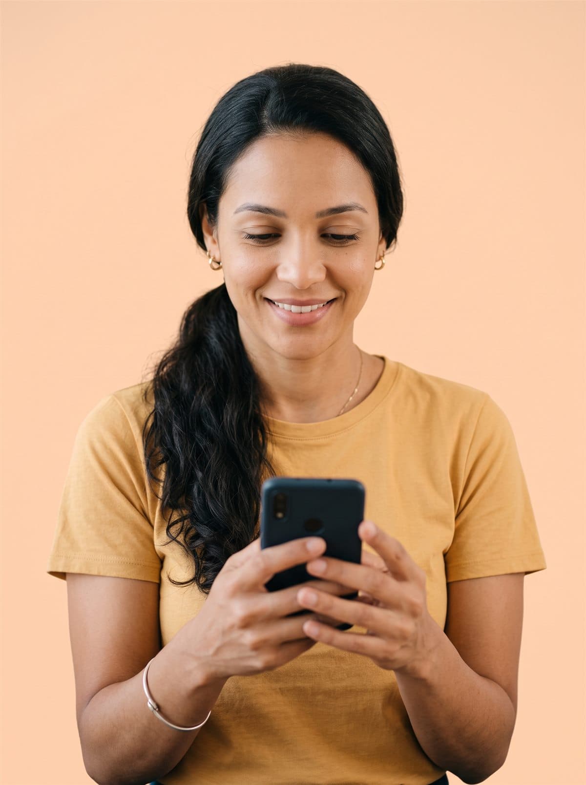 Imagem ilustrativa: mulher de camiseta amarela, sorrindo enquanto olha o celular